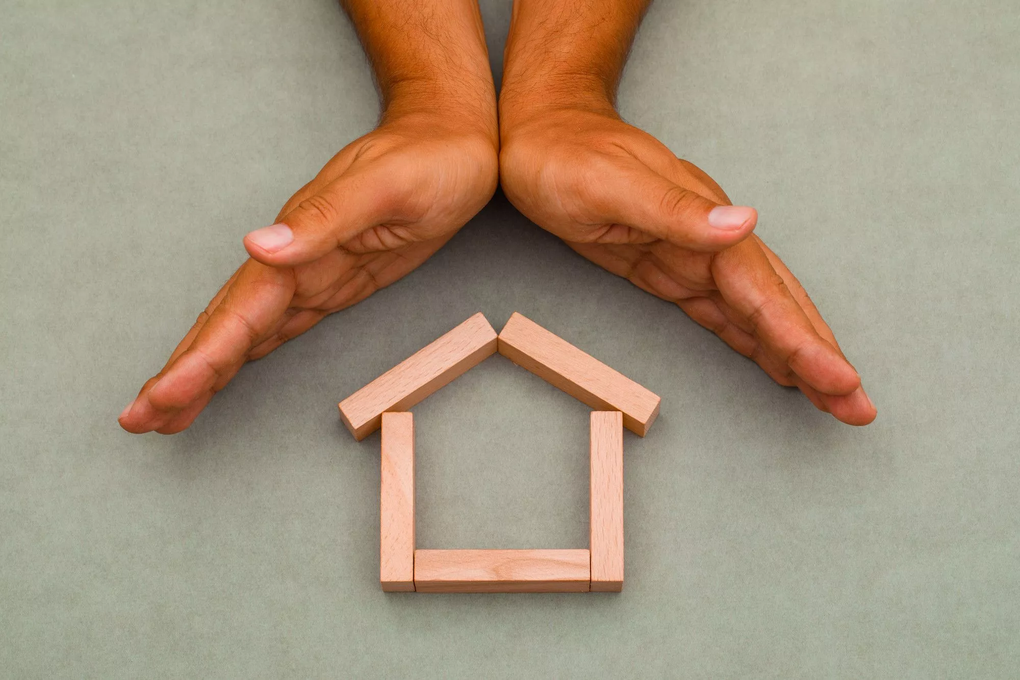 An Image of # Blocks Of Wood Creating A Mini House Symbol With Human Hands Above It